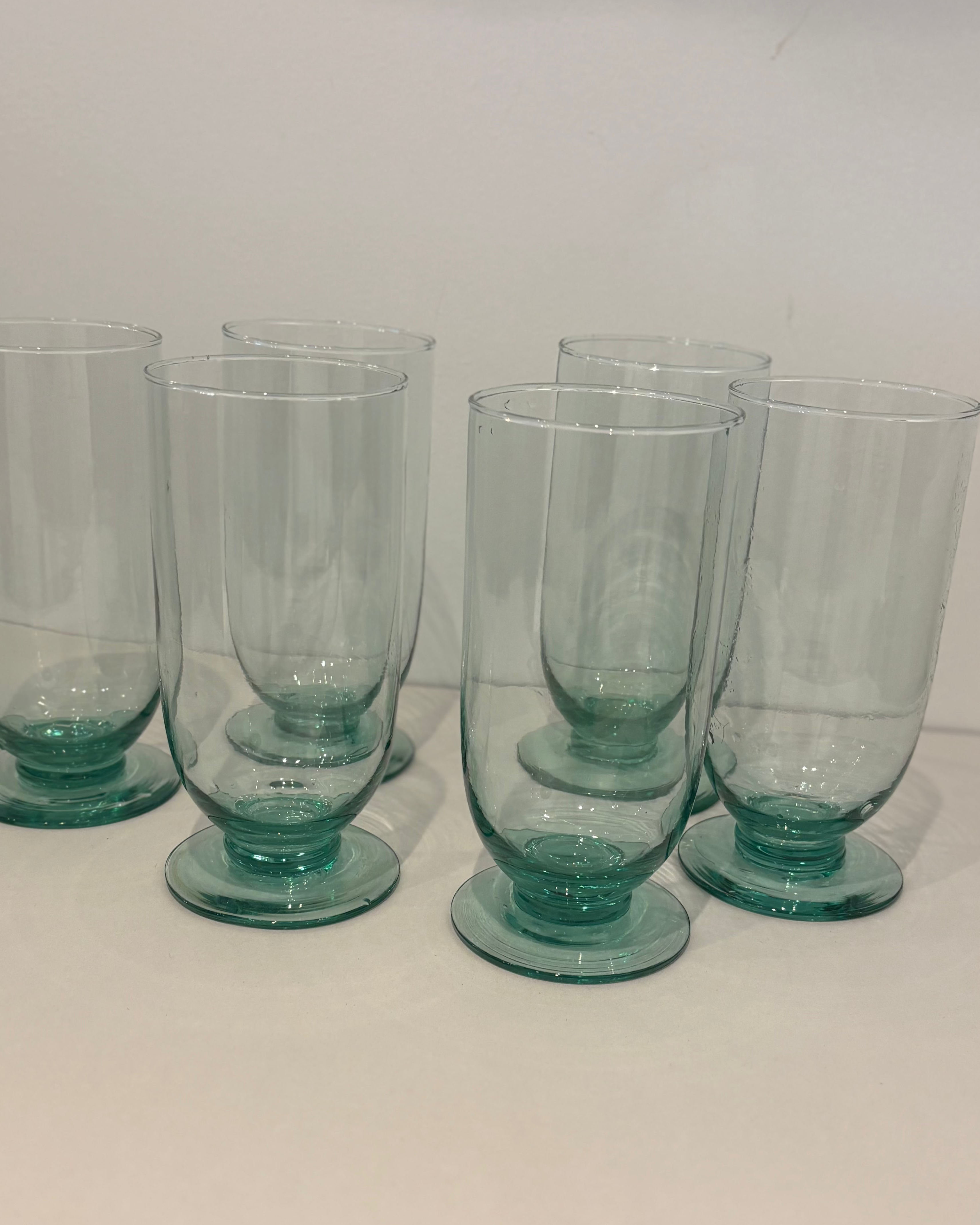 Set of six teal glass tumblers on a white surface with a white background
