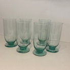 Set of six teal glass tumblers on a white surface with a white background