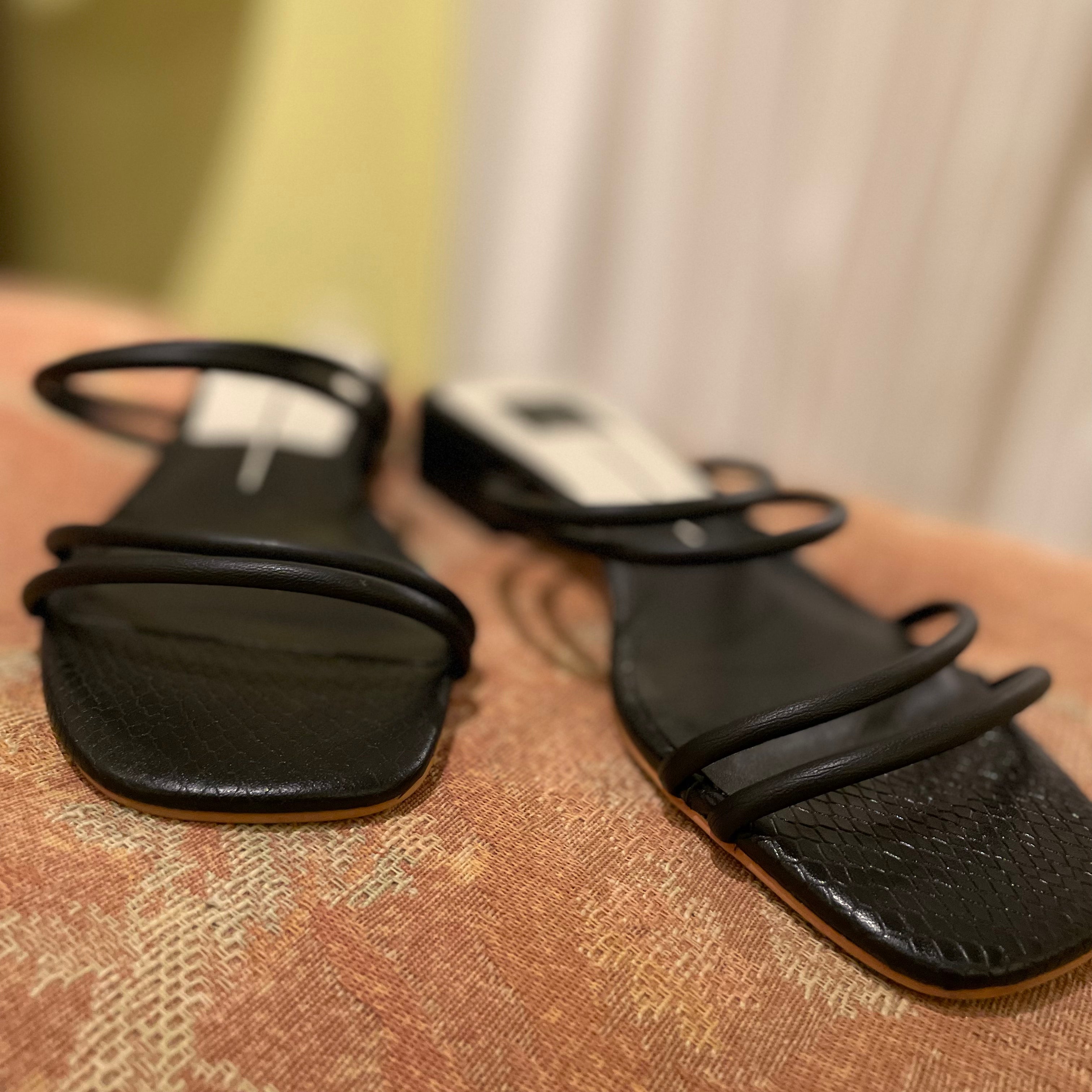 Black sandals with thin straps on a textured surface